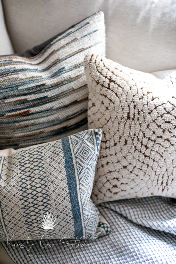 Close up of multiple textured decorative pillows on couch in living room.